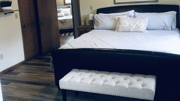 Un dormitorio con cama, ventilador de techo, mesita de noche y una imagen enmarcada en la pared, además de una puerta que da a otra habitación.