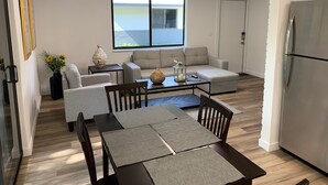 Een moderne woonkamer met een bank, salontafel en een eettafel. Een groot raam biedt uitzicht op het omliggende landschap.