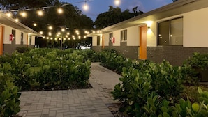 Een hotelgang met een metselpad, lichtslingers en beplanting.