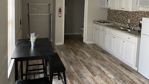 A kitchen with white cabinets, a black countertop, and a wooden floor. There is a dining table with chairs and a small plant on it. A fire extinguisher is mounted on the wall. - Family Vacation Cabin C3 (Cleveland)
