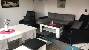 Ein modernes Wohnzimmer mit grauem Sofa, schwarzen Sesseln, einem weißen Couchtisch und einer schwarzen Stehlampe.