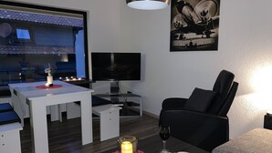 Ein modernes Wohnzimmer mit Essbereich, einem schwarzen Ledersessel, einem Glastisch mit Kerze, einem Weinglas und einem gerahmten Bild an der Wand.