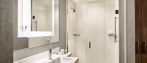 A modern bathroom with a large mirror, two sinks, a shower, and a walk-in shower stall.