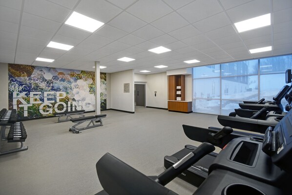 Un gimnasio con cintas de correr, bicicletas estáticas y un mural con mensajes motivacionales.