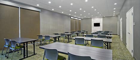 Un salón de conferencias con mesas y sillas, un televisor de pantalla plana y suelo alfombrado.