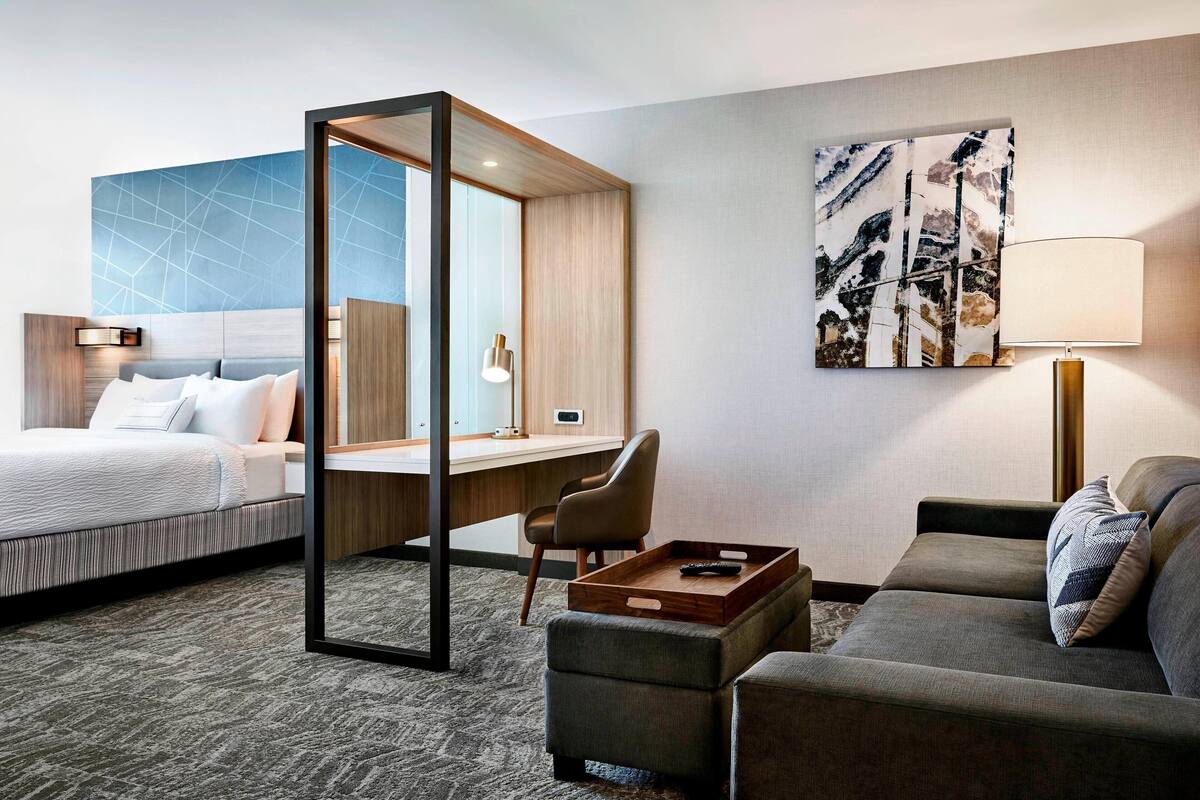 A hotel room with a bed, a desk, a sofa, and a large abstract painting on the wall.
