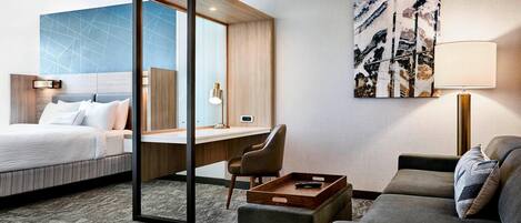 Ein Hotelzimmer mit Bett, Schreibtisch, Sofa und einem großen, abstrakten Gemälde an der Wand.