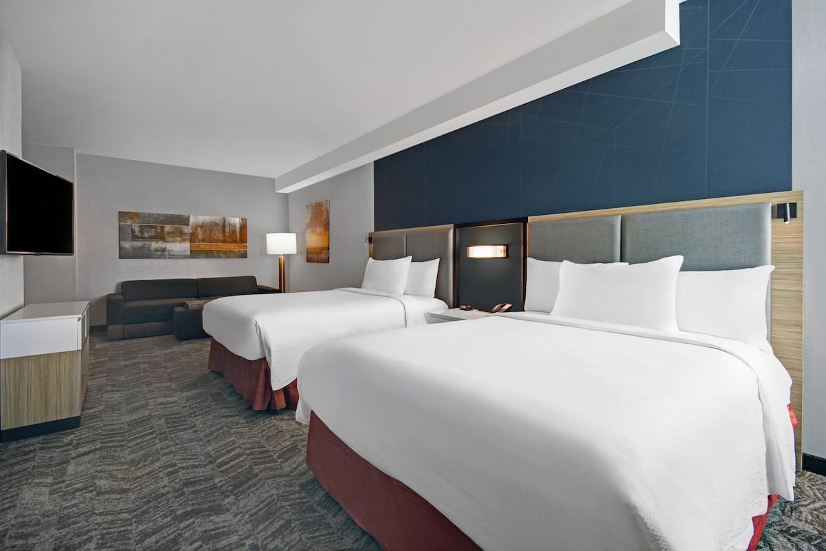 A hotel room with two beds, a sofa, a TV, and artwork on the walls.