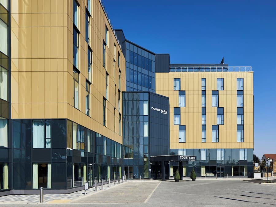A modern hotel with a courtyard, large glass windows, and a mix of beige and dark-colored facades.