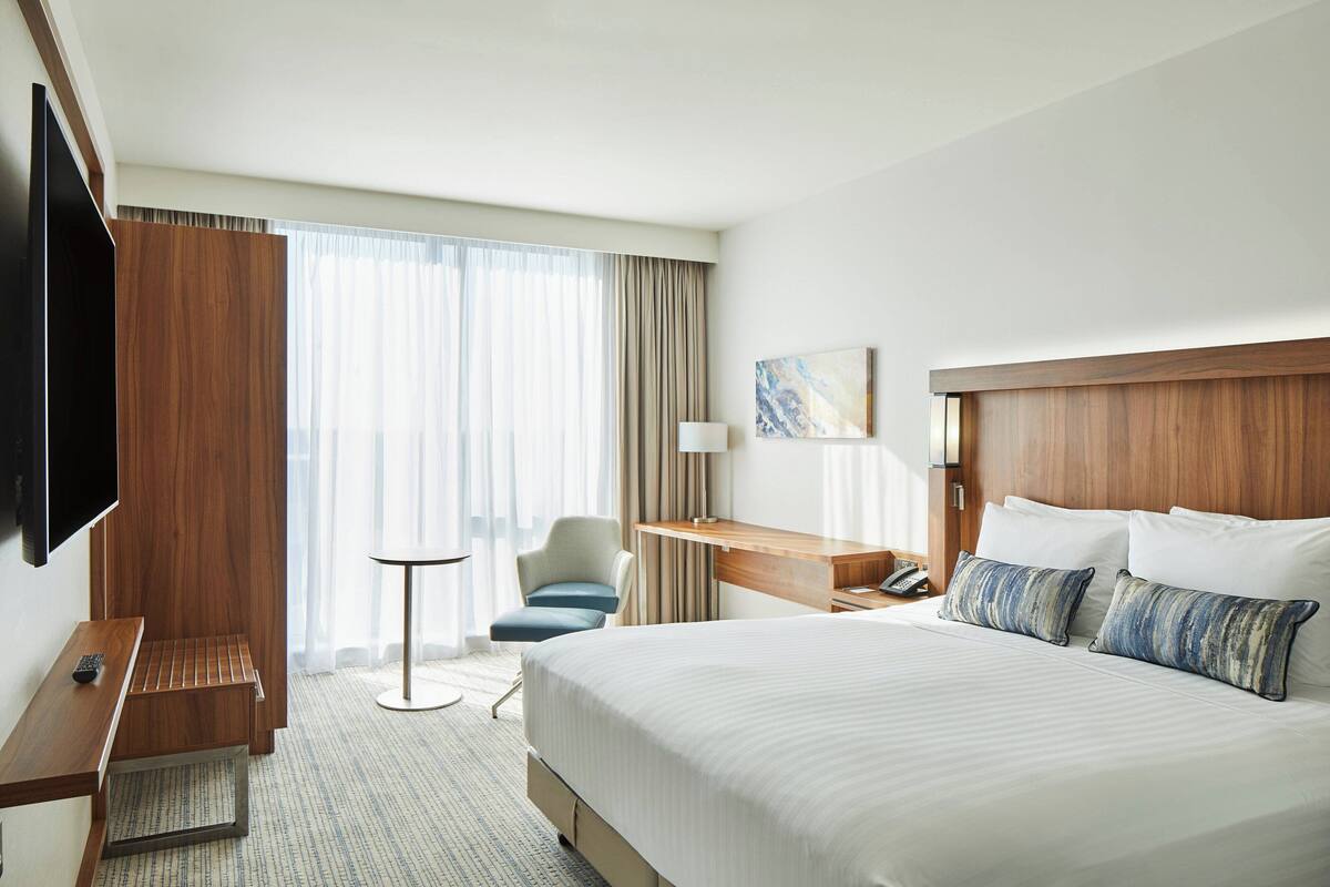 A hotel room with a large bed, a desk, a chair, a TV, and a window with curtains.