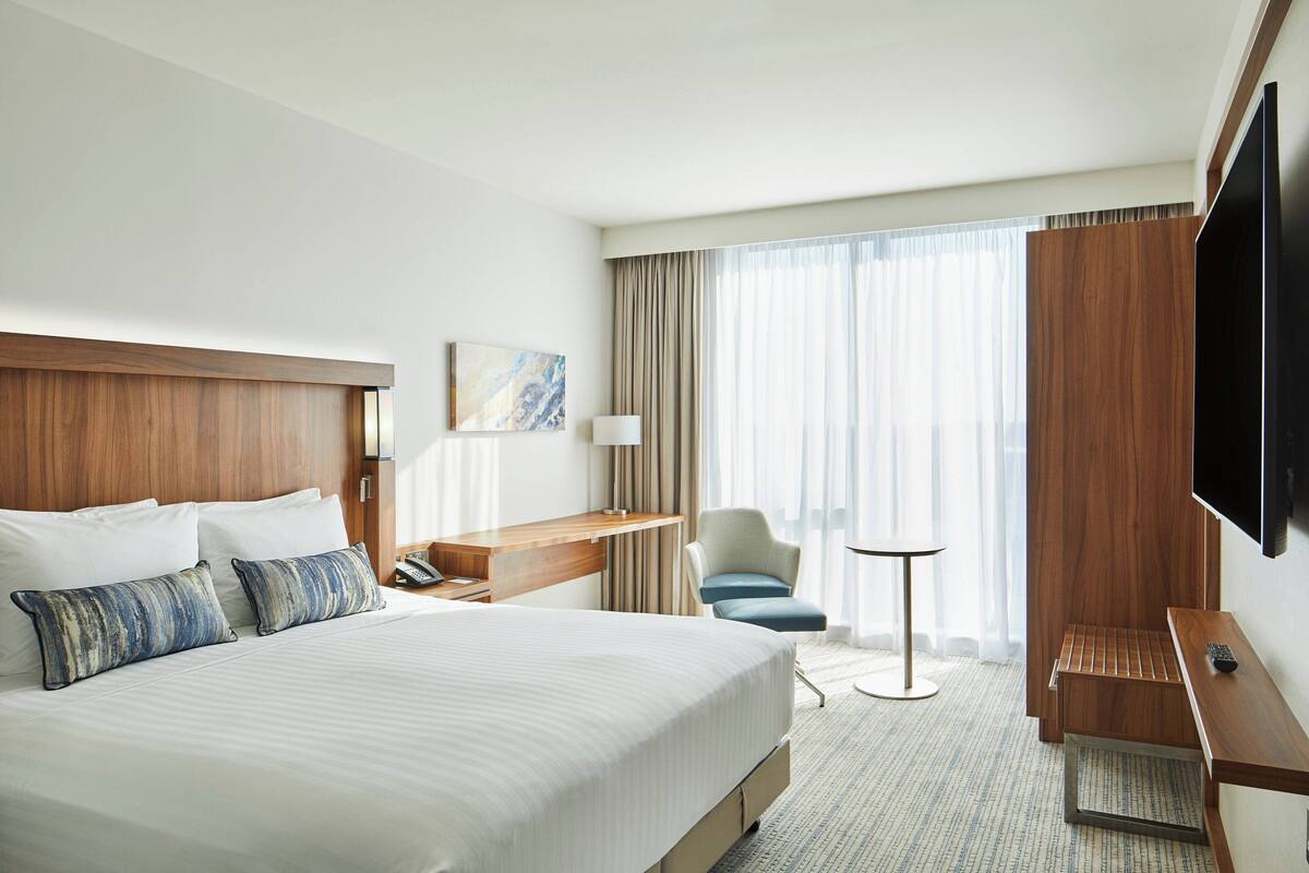 A hotel room with a large bed, a desk, a chair, a TV, and a window with curtains.