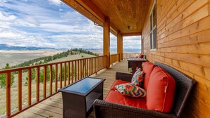 A wooden deck with a sofa and table, overlooking a mountainous landscape. - The Lodge at Arcady Ridge Ranch, SWIM SPA + SAUNA sleeps up to 14! (Dubois)