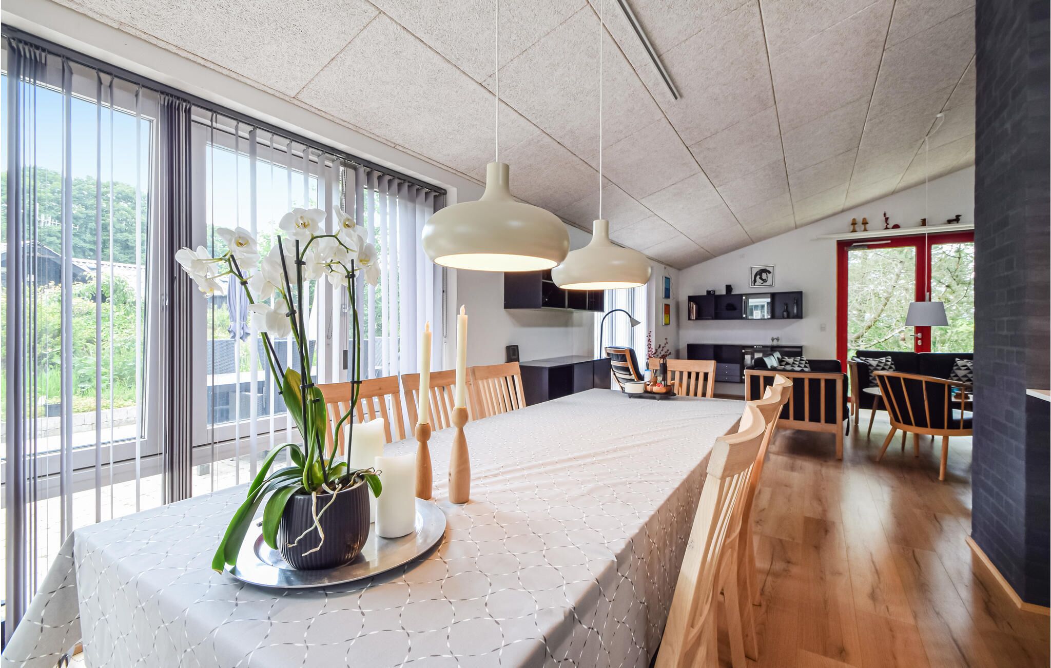 Un espace de salle à manger moderne, avec une longue table, des suspensions blanches et une plante orchidée en pot.