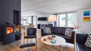 Moderni olohuone, jossa on takka, sohva, ruokailutila ja suuret ikkunat.