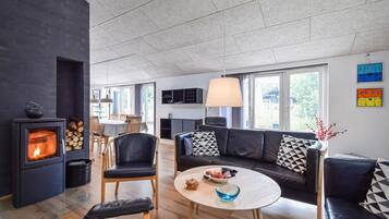 Un salon moderne doté d’une cheminée, d’un canapé, d’un coin repas et de grandes fenêtres.