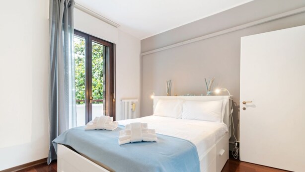 Una camera da letto con un letto, una finestra con tende, un termosifone e una porta.