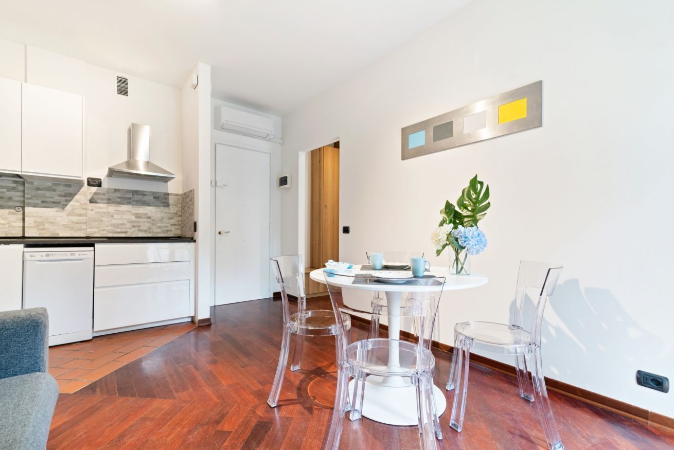 A modern kitchen with white cabinets, a stainless steel range hood, and a dining area with a round table and clear chairs.