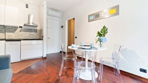Una cucina moderna con mobili bianchi, una cappa aspirante in acciaio inossidabile e un'area pranzo con un tavolo rotondo e sedie trasparenti.