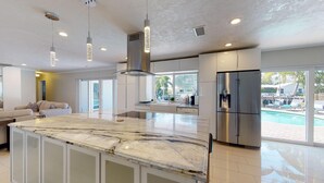 Een moderne keuken met een marmeren eiland, roestvrijstalen apparatuur en een groot raam met uitzicht op een zwembad.