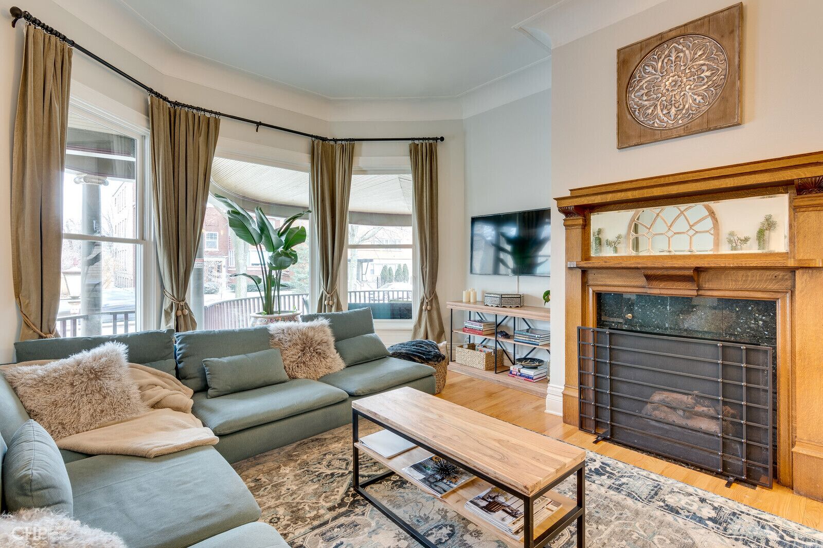 A living room with a sofa, coffee table, and fireplace. There is a TV mounted on the wall and a plant in the corner.