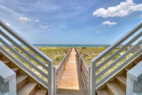 A wooden boardwalk leading to a beach with a clear sky.