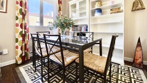 Uma sala de jantar com mesa de vidro, cadeiras de fibra natural e tapete estampado.