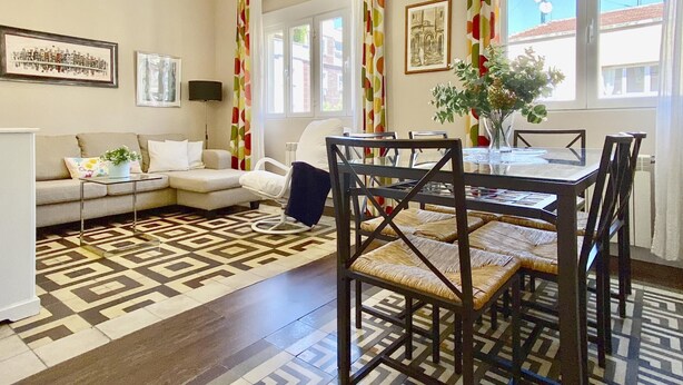 Uma sala de estar moderna com área de jantar, destacando um tapete estampado, um sofá, uma mesa de centro e uma mesa de jantar com cadeiras.