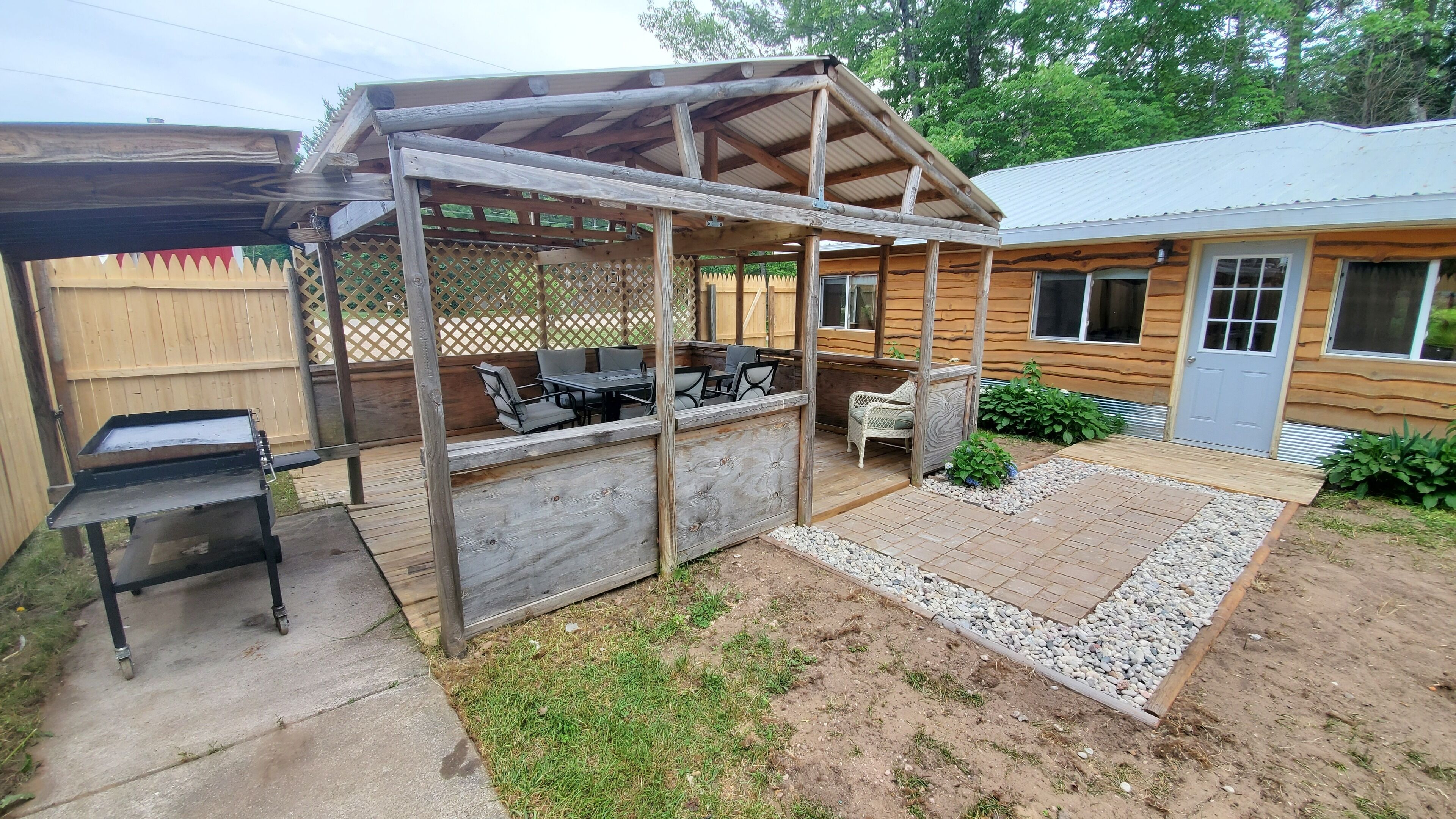 A wooden outdoor patio with a grill, seating, and a covered area.