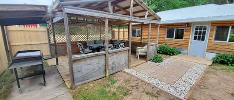 A wooden outdoor patio with a grill, seating, and a covered area.