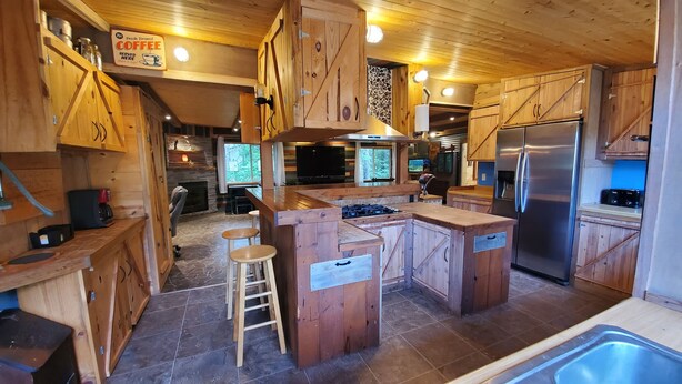 Une cuisine rustique avec des meubles en bois, un îlot central doté de tabourets, une cuisinière encastrée et un réfrigérateur en acier inoxydable.