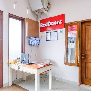 A reception area with a RedDoorz sign, a desk with a computer, a television, and a door with a WiFi sign. - OYO 3314 Syariah House (Purwokerto)