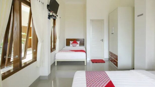 A bedroom with a bed, a wardrobe, a television mounted on the wall, and a window with curtains. - OYO 3314 Syariah House (Purwokerto)
