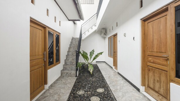 A hallway with a staircase, wooden doors, and a potted plant. - OYO 3267 Omah Suryo (Yogyakarta)