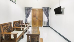 A room with a wooden dining table, four wooden chairs, a TV mounted on the wall, and a door with curtains. - OYO 3267 Omah Suryo (Yogyakarta)