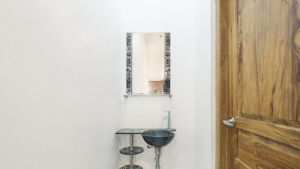 A bathroom with a wooden door, a wall-mounted mirror, and a sink with a black basin and two round, patterned shelves below it.