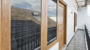 A corridor with a wooden door and a window, leading to a balcony with a tiled roof. - OYO 3267 Omah Suryo (Yogyakarta)