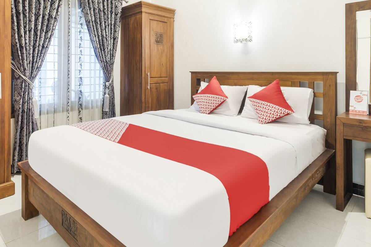 Un lit bien fait, recouvert d’une couvre-lit rouge et blanche, avec une tête de lit en bois et deux oreillers rouges ornés de motifs blancs.