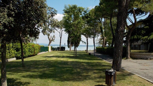 A grassy area with trees and a trash bin. - Aura Home Sirmione - 2 bedrooms apartment (Sirmione)