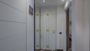 A hallway with a white door with yellow accents, a small mirror on the wall, and a tiled floor. - Aura Home Sirmione - 2 bedrooms apartment (Sirmione)