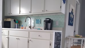 Una cocina con armarios blancos, una cafetera y un menú en pizarra.