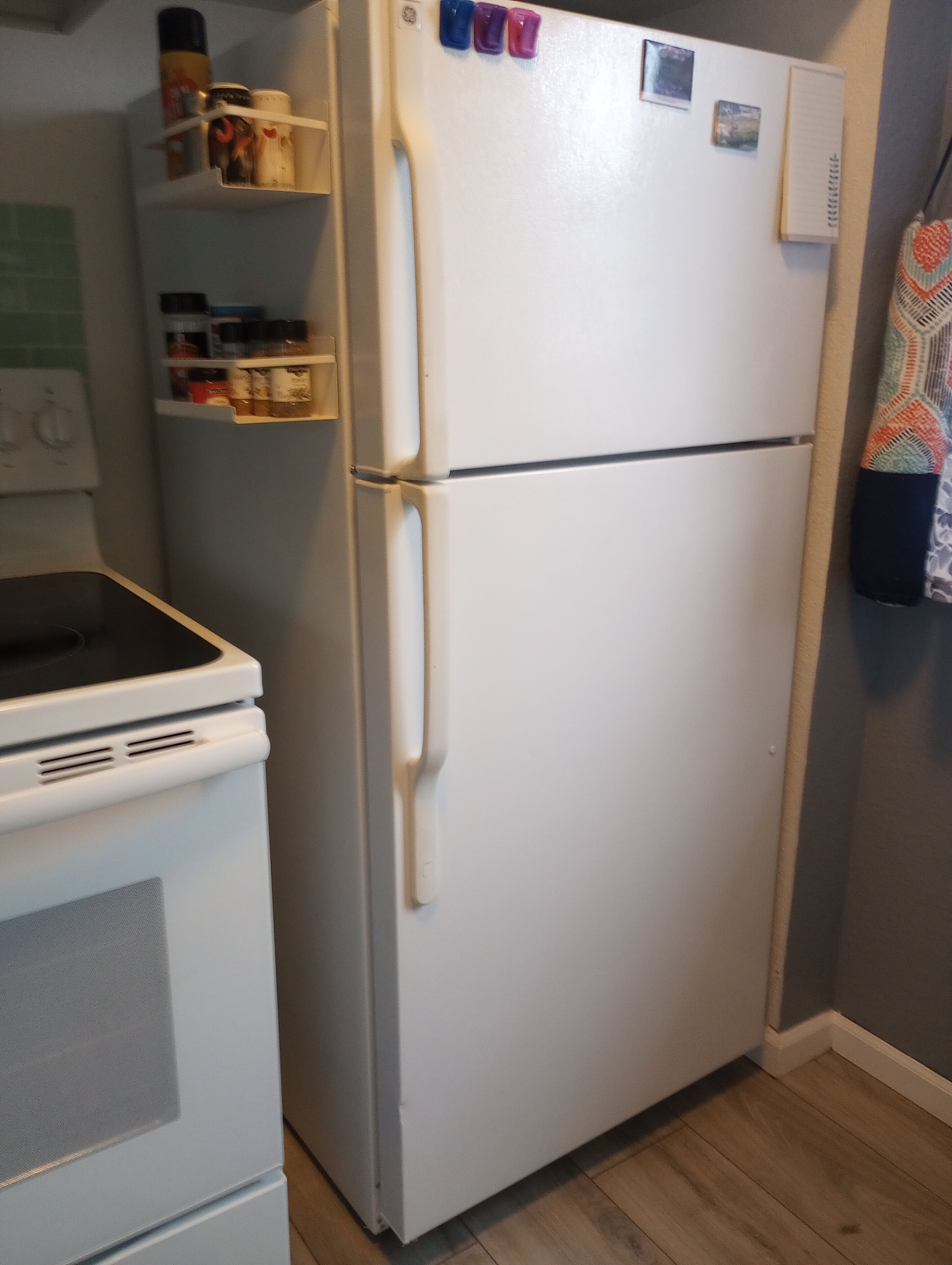 Una cocina con un refrigerador blanco, una estufa y un microondas. Hay repisas sobre el refrigerador con varios objetos.