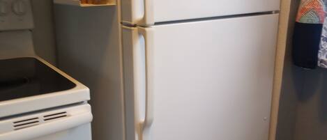 Una cocina con un refrigerador blanco, una estufa y un microondas. Hay repisas sobre el refrigerador con varios objetos.