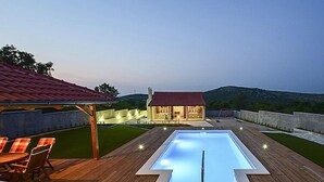 Eine Holzterrasse mit Pool, Sitzgelegenheiten im Freien und einem Gebäude mit rotem Dach.