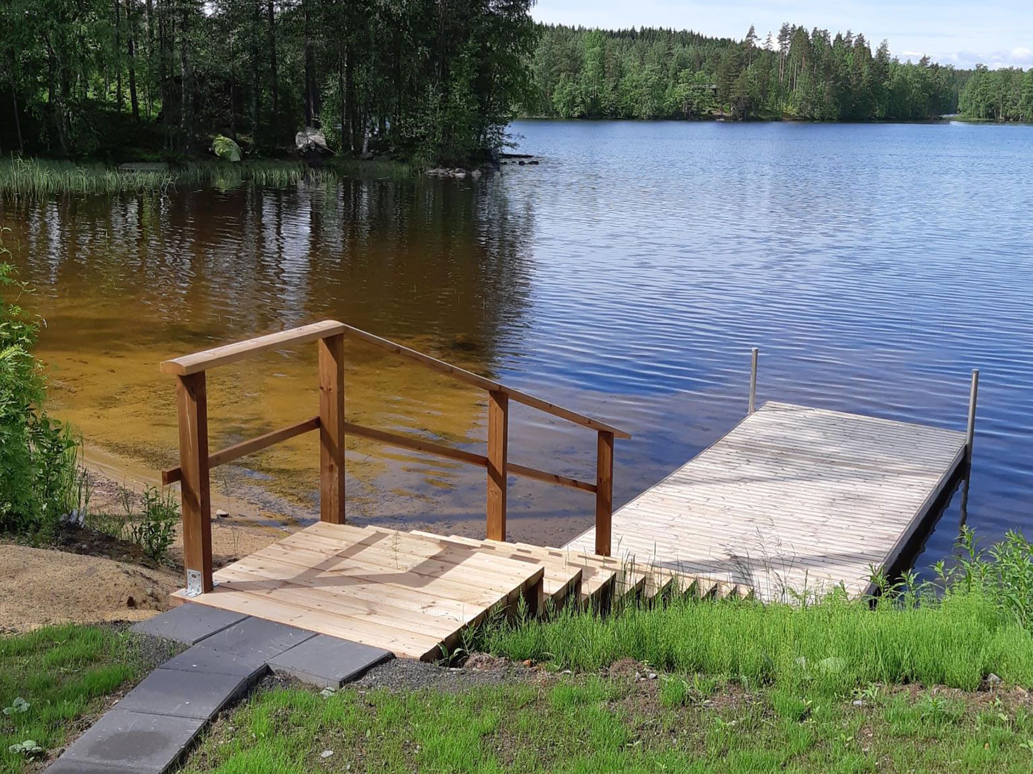 En träbrygga som sträcker sig ut i en stilla sjö, omgiven av tät skog.