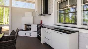 Una cocina compacta con armarios blancos, un extractor de humos negro y un amplio ventanal con vistas a árboles.