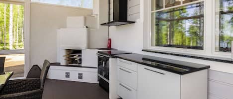Cuina compacta amb armaris blancs, una campana extractora negra i una finestra gran amb vista a arbres.