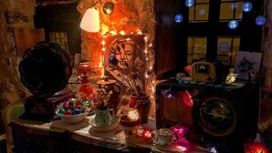 A dimly lit room with a rustic stone wall, a vintage gramophone, and various decorative items including a Buddha statue, candles, and a framed picture.