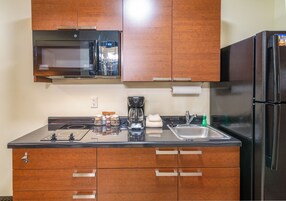 Una cocina con armarios de madera, un refrigerador negro, un microondas, una cafetera y un lavamanos.