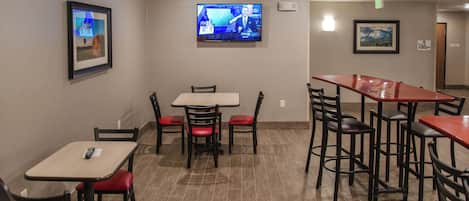 A restaurant with tables and chairs, a television mounted on the wall, and framed pictures on the walls.