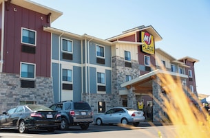A multi-story hotel with a stone facade and a 'My Place Hotels' sign. There are cars parked in front and a group of people near the entrance.